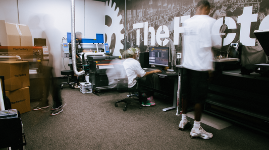People working at computers in an office with 'The Factory' branding on the wall.